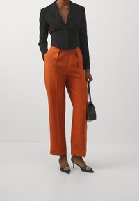 Black cropped blazer, orange high-waisted pants, black pointed-toe heels with decorative hardware, and a small black handbag.