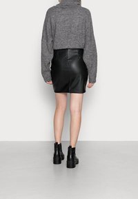 Un maglione grigio a maglia con colletto alto è abbinato a una minigonna in pelle nera. Stivali neri alla caviglia con suole spesse completano il look.