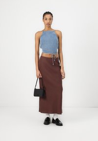Denim crop top with adjustable ties, brown high-waisted skirt, black mini handbag, white socks, and black shoes. Smooth textures, minimalist design.