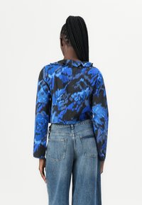 Blusa corta con motivo astratto blu e nero, con maniche lunghe e colletto arricciato, abbinata a jeans in denim a vita alta.