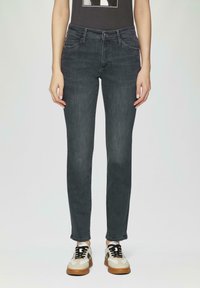 Jean en denim gris foncé à coupe slim, avec des détails de poches discrets et des ourlets légèrement effilochés, associés à des baskets beige et noires.