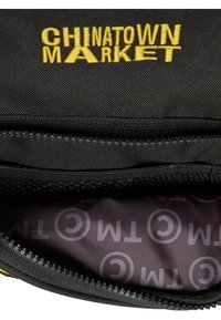 Sort tekstilpose med gul "CHINATOWN MARKET" broderi, med lynlås og et mønstret indre med lys grå logoer.
