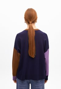 Sweter dzianinowy z kolorowym wzorem w odcieniach granatu, brązu i fioletu, z okrągłym dekoltem i ściągaczami. Nosi się go z dżinsami.