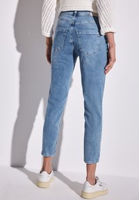 Vaqueros de mezclilla azul claro con corte ajustado, cinco bolsillos y un diseño sencillo. Presentan una cintura de altura media y un dobladillo sin terminar en los tobillos.