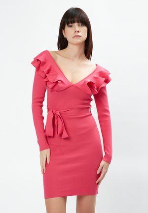 Abito rosa a coste con scollatura a V profonda, dettagli arricciati sulle spalle e vita legata. Maniche lunghe e silhouette aderente.