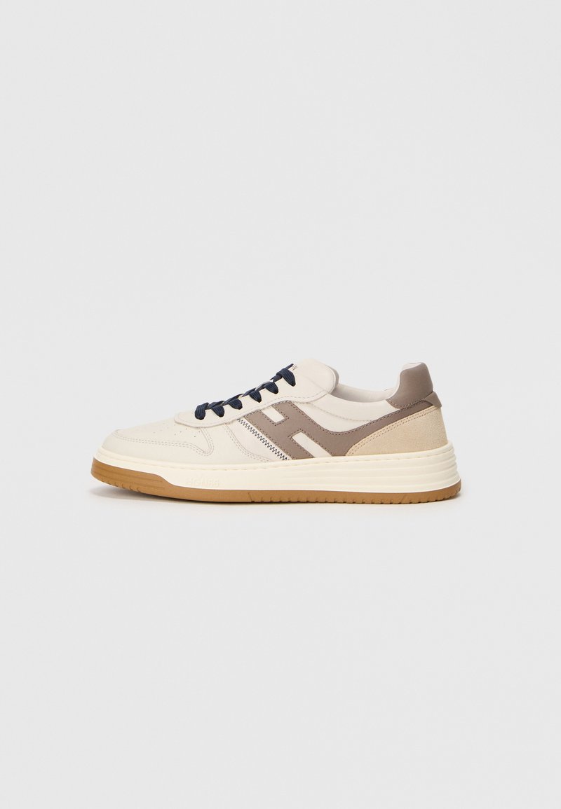 Sneakers with a cream leather upper, brown suede accents, and a dark blue lace system. Features flat rubber sole with textured grip.