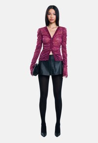 Burgundy lace-toppi, jossa on ryppyiset pitkät hihat, v-pääntie ja napit, yhdistetty mustaan nahkahameeseen ja mustiin sukkahousuihin.