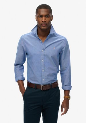 Blauwe button-up shirt met een kraag en opgerolde mouwen, voorzien van een klein geborduurd logo. Draag het met donkere broeken en een leren bruine riem.