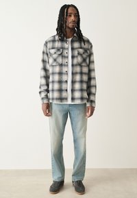 Camicia in flanella a quadri bianco e nero con due tasche sul petto, abbinata a jeans azzurri e sneakers grigie. Tessuto morbido e casual.