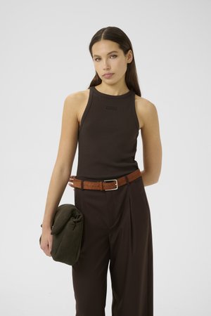 Brown ribbed tank top with a round neckline, paired with high-waisted tailored pants and a brown belt. Holding a green folded bag.