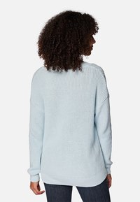Himmelblaues Strickoberteil mit lässiger Passform, geripptem Halsausschnitt und Bündchen sowie einem leicht längeren Rückensaum, kombiniert mit dunklen Jeans.