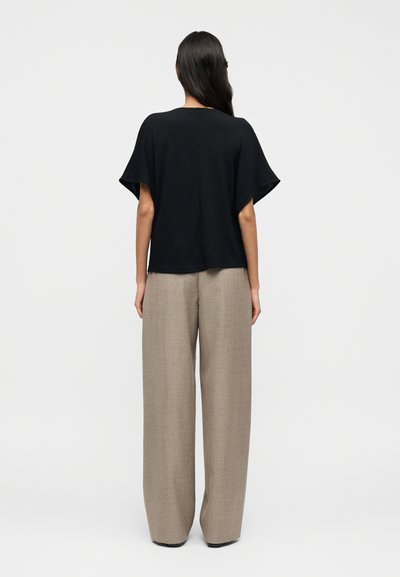 Μαύρο κοντομάνικο τοπ με άνετη εφαρμογή, σε συνδυασμό με μπεζ παντελόνια ψηλόμεσα και φαρδιά, κατασκευασμένα από υφασμάτινο ύφασμα με υφή.