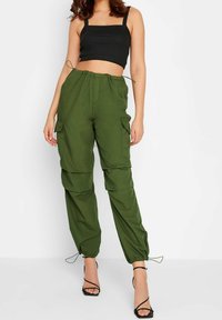 Grüne Cargo-Hosen aus leichtem Stoff, mit verstellbaren Kordelzug-Bündchen und mehreren Seitentaschen. Getragen mit einem schwarzen Crop-Top.