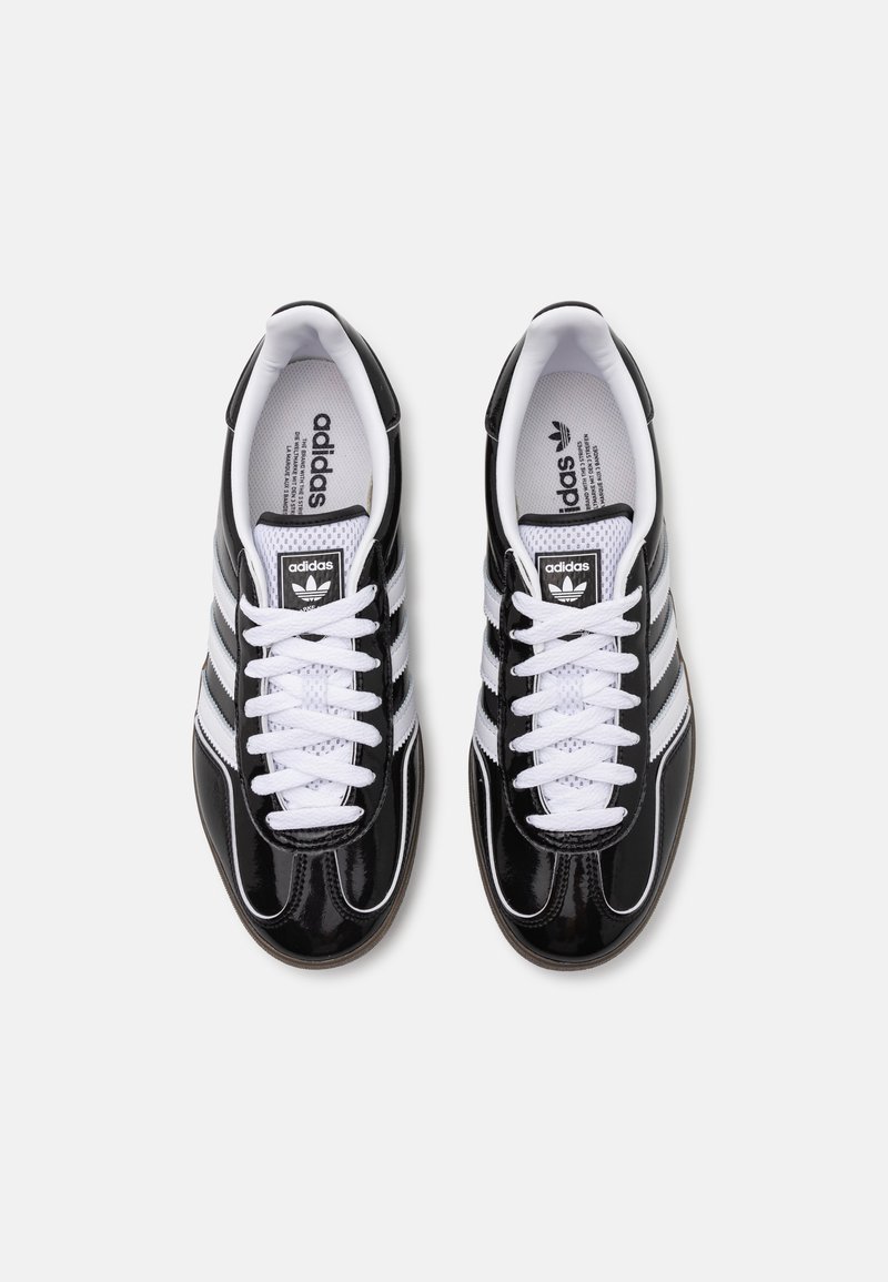 Czarne sneakersy z lakierowanej skóry z białą siateczką, z trzema białymi paskami, białymi sznurówkami i czarną metką z logo na języku.