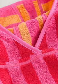 Handtuch mit abwechselnden rosa und orangen Streifen, hergestellt aus Frottierstoff mit weicher Textur. Die Ränder sind mit einer rosa Einfassung abgeschlossen.