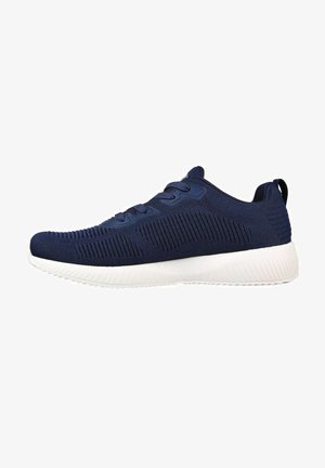 Zapatilla deportiva de color azul marino con parte superior de punto texturizado, suela blanca y acabado suave. Presenta líneas curvas y una pestaña en el talón.