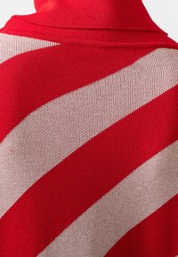 Vêtement tricoté rouge présentant de larges rayures diagonales en ivoire, avec un tissu texturé et un design de col montant à l'arrière.