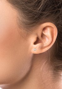 Pendiente de oro con diseño cuadrado y una gema redonda clara. Llevado en la oreja, mostrando la simple elegancia del pendiente.