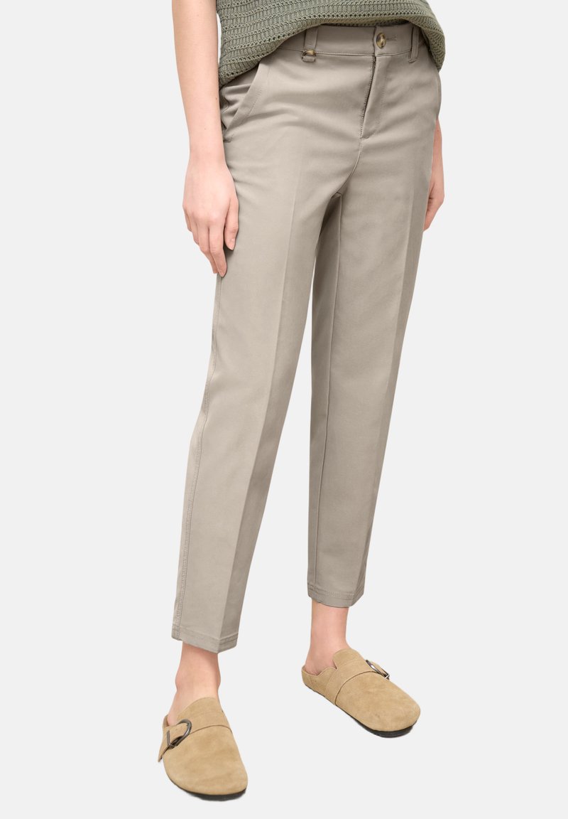 Pantalones beige de pierna recta combinados con zapatos tipo slip-on de ante color camel con hebilla, en una persona de pie frente a un fondo liso.
