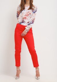 Camicia a maniche lunghe floreale con pantaloni rossi aderenti. La camicia presenta una combinazione di colori rosa, blu e crema. Scarpe con tacco alto argentate.
