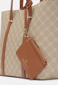 Beige kantokassi, jossa on kohoavuuskuvio, ruskeat nahkahandleet ja siihen kiinnitetty yhteensopiva pieni vetoketjullinen lompakko kultaisella klipsillä.