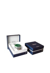 Montre en acier inoxydable argenté avec un cadran vert dans une boîte ouverte bleu marine. La montre présente de grands index horaires blancs et un bracelet métallique.