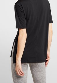 Camiseta negra de manga corta con un corte relajado, aberturas laterales y una textura suave, combinada con leggings ajustados en gris claro.