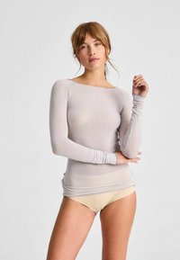 Helles graues Langarmshirt aus weich dünnem Material. Verfügt über einen weiten Ausschnitt und eine taillierte Form, mit betonten Handgelenkbündchen.