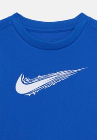 Blå atletisk skjorte laget av teksturert stoff har en hvit Nike swoosh-logo med et dynamisk design, rund halslinning og korte ermer.