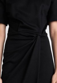 Abito nero con maniche corte, dettagli a nodo torcigliato in vita e una texture di tessuto morbido, che crea una silhouette elegante.