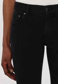 Svarta denimjeans med hög midja, femficksdesign, silvriga detaljer och en slät yta, fångade från midjan och ner.