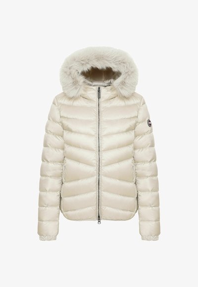 Veste d'hiver matelassée de couleur crème avec une fermeture éclair à l'avant et une capuche doublée en fourrure, avec un petit patch logo rond sur la manche gauche.