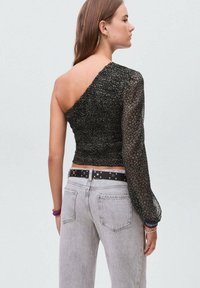Top nero con design a spalla unica; tessuto strutturato con un delicato motivo; manica lunga trasparente; abbinato a jeans grigi chiari e una cintura stellata.