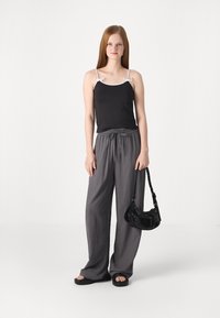 Svart cami-top med hvite stropper, grå vide bukser, svart skulderveske, flate svarte sandaler med teksturert såle. Renslig, minimalistisk design.