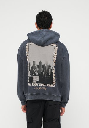 Bluza z kapturem w ciemnoszarym kolorze z dużą grafiką krajobrazu miejskiego z tyłu, z tekstem i kontrastowymi kremowymi akcentami. Materiał z mieszanki bawełny.