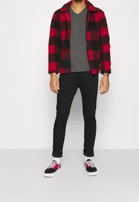 Czerwono-czarna, w kratę, polarowa kurtka, szary T-shirt w serek, czarne dżinsy i czarne trampki Vans z czerwonymi akcentami. Posiada standardowy krój.