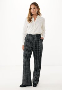 Vit skjorta med knappar kombinerad med svartvitt mönstrade vida byxor, med elastisk midja och sidofickor, kompletterat med svarta skor.