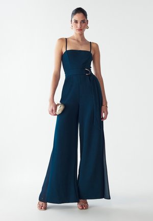Navyblauer Jumpsuit mit taillierter Passform, dünnen Trägern und weitem Bein. Ausgestattet mit einem Gürtel mit einer runden Schnalle und einer glatten Stofftextur.