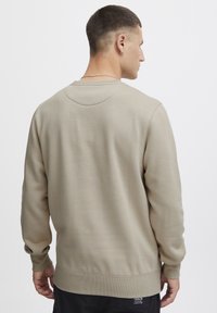 Sudadera beige con cuello redondo y puños acanalados, hecha de una tela suave. Presenta un corte holgado y sutiles detalles de costura en la parte posterior.
