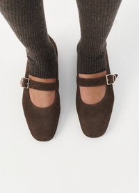 Scarpe Mary Jane in suede marrone con punta rotonda, fascia a metà piede con fibbia argentata, abbinate a calze scure a coste.