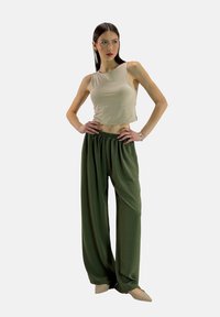 Beige cropped tanktop gecombineerd met losse, hooglopende olijfgroene broek. De outfit heeft een ontspannen pasvorm en een zachte textuur.