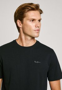 Černé bavlněné tričko s kulatým výstřihem a krátkými rukávy, s malým bílým logem "Pepe Jeans" na levé části hrudníku.