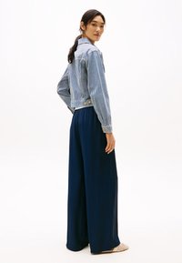 Blå og hvitstripet avkortet denimjakke med knapper, kombinert med marineblå vide bukser i glatt stoff. Elegant uformell stil.