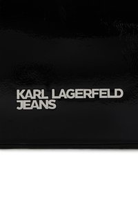 Svart texturerad yta med silverfärgad "KARL LAGERFELD JEANS"-logotyp. Bokstäverna är i fet stil och versaler, vilket kontrasterar mot bakgrunden.