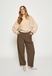 Bēšas teksturētas džemperis ar izlaidīgiem pleciem, apvienots ar brīvā stilā izgatavotām tumši brūnām ērtiem biksēm. Ar izteiksmīgiem bēša augstpapēžu apaviem papildināta šī tērpa noslēgšana.