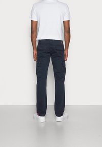 Námořnicky modré cargo kalhoty s několika bočními kapsami, rovný střih nohavic a mírný lesk. Kombinovány s jednobarevným bílým tričkem a bílými teniskami.