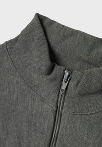 Veste à zip gris foncé avec un col haut, tissu texturé et fermeture éclair robuste. Lignes épurées et design minimal.