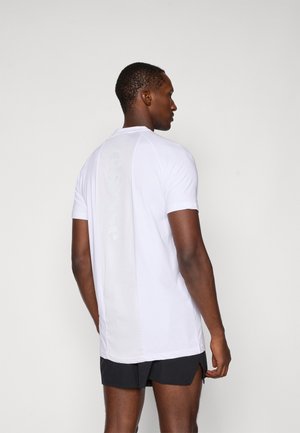 White athletic t-shirt featuring a mesh back with a logo, short sleeves, and a regular fit, paired with black shorts.