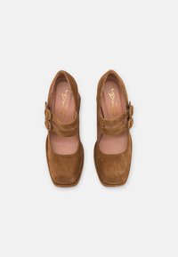 Brune Mary Jane-sko i ruskind med firkantet tå, to runde spænderemme og en glat inderforing. Flad hældesign.