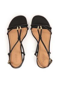 Sandali in pelle nera con suola piatta, caratterizzati da un delicato design delle cinghie e dettagli in metallo dorato. Soletta liscia color tabacco con nome del marchio.